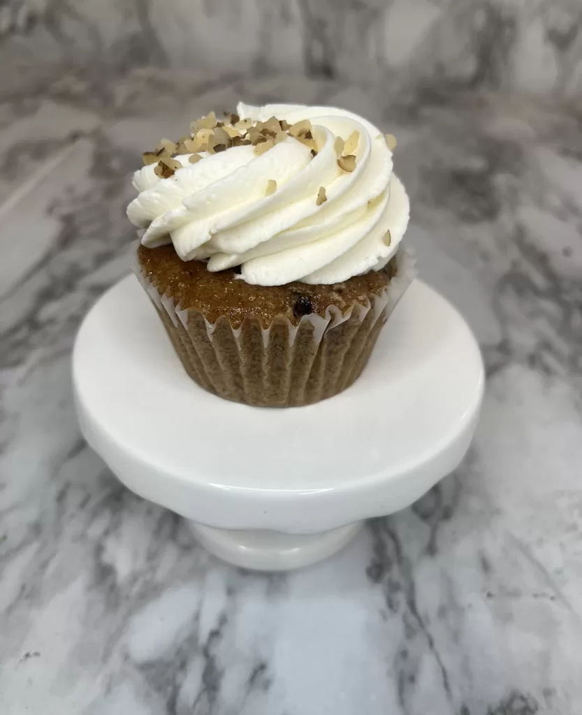 Carrot cupcake garnished with chopped and crushed pecans on top.